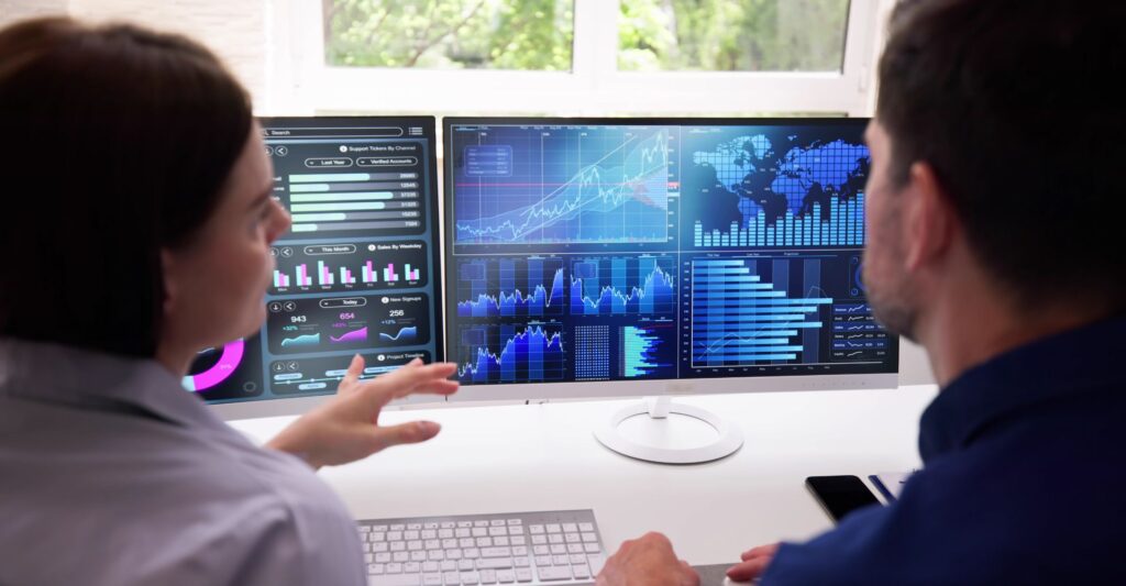 people sitting at desk look at screens with graphs